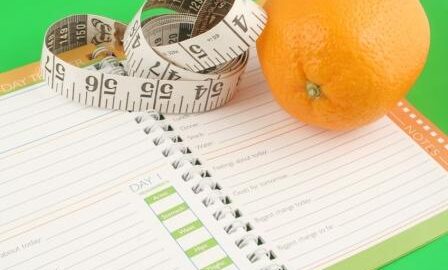 a measuring tape, diet and nutrition journal and an orange