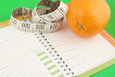 a measuring tape, diet and nutrition journal and an orange
