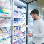 A man chooses frozen foods from shelves in a refrigerator in a supermarket. A man buys products in the store. Shopping in a supermarket concept.
