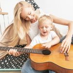 Music In Childhood Health Benefits Little boy playing on guitar with mom .