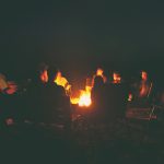 The group of friends are sitting near the bonfire in the night a